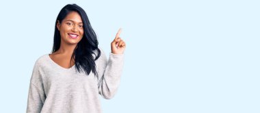 Uzun saçlı, sıradan kıyafetler giyen, yüzünde kocaman bir gülümseme olan İspanyol kadın, kameraya el ile işaret ediyor.. 