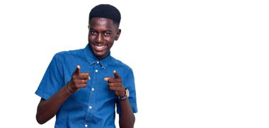 Sıradan kıyafetler giymiş genç Afro-Amerikalı adam mutlu ve komik yüzüyle kamerayı işaret ediyor. iyi enerji ve titreşimler. 