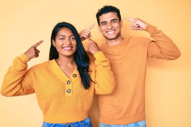 Güzel Latin bir çift, günlük kıyafetlerini giyip gülümsüyor. İki eliyle kafasını işaret ediyor. Harika bir fikir ya da düşünce, iyi bir hafıza. 