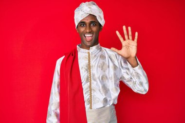 Yakışıklı Hintli adam geleneksel Sherwani sari giysisi giyer ve parmaklarıyla 5 numarayı göstererek gülümserken kendinden emin ve mutlu. 