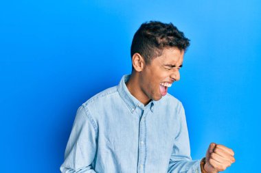 Genç, yakışıklı, Afro-Amerikan bir adam gündelik giysiler içinde kolları havada ve gözleri kapalı bir şekilde başarıyı kutluyor. 