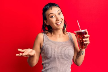 Bir bardak kola içen genç kadın başarıyı mutlu bir gülümsemeyle ve kazanan yüz ifadesiyle kutluyor. 