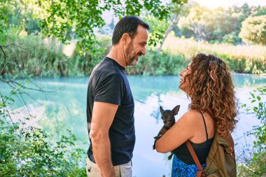 Orta yaşlı bir çift, günlük giysiler giyip parkta Chihuahua köpeği tutuyorlar.