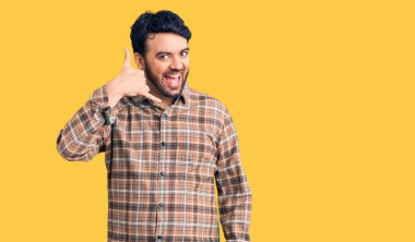 Günlük kıyafetler giymiş, gülümseyen genç İspanyol adam telefonla el ve parmak hareketleri yapıyor telefonda konuşur gibi. iletişim kavramları. 