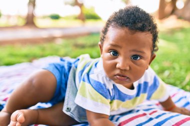 Sevimli Afro-Amerikan çocuk parkta çimlerin üzerinde oturuyor..