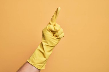 İzole edilmiş sarı arka plan üzerinde temizlik eldiveni olan beyaz bir gencin eli işaret parmağı kullanarak bir numarayı sayıyor, fikir ve anlayış gösteriyor.