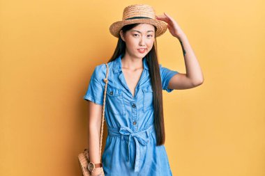 Yaz şapkası takan genç Çinli kadın soru sorup şaşırıyor. Şüpheyle kararsız, kafa kafaya düşünerek. Düşünceli kavram. 