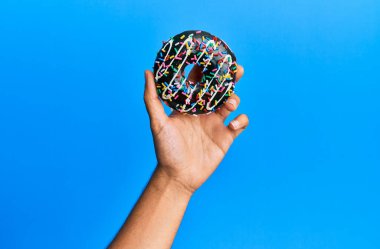 İzole edilmiş mavi arka planda çikolatalı çörek tutan İspanyol bir adam..