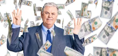 İş ceketi giyen yaşlı gri saçlı adam dokuz numarayı gösterip işaret ederken kendinden emin ve mutlu bir şekilde gülümsüyor..