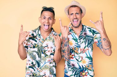 Yazlık şapkalı ve Hawaii tişörtlü iki genç eşcinsel çılgın bir ifadeyle elleri havada rock sembolü yaparak bağırıyor. Müzik yıldızı. ağır müzik konsepti. 