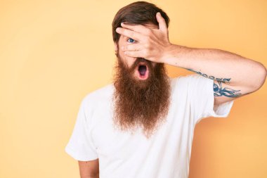 Uzun sakallı, beyaz tişörtlü yakışıklı genç adam. Şok olmuş, yüzünü ve gözlerini kapamış, parmaklarından korkuyla bakıyor. 