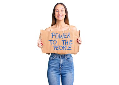 Güzel, esmer, genç bir kadın elinde güç, afiş, pozitif ve mutlu görünüyor. Kendine güvenen bir gülümsemeyle, dişlerini gösteriyor. 