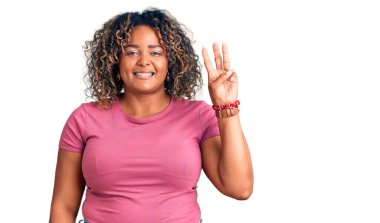 Genç Afro-Amerikan artı cüsseli kadın rahat kıyafetler giyiyor ve üç numaralı parmaklarıyla işaret ederken kendinden emin ve mutlu gülümsüyor.. 