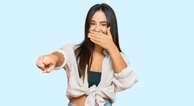 Gündelik giysiler içinde genç ve güzel bir İspanyol kız sana gülüyor, eli ağzında kamerayı işaret ediyor, utanç ifadesi var. 