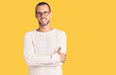 Sıradan kıyafetler giyen, gözlüklü mutlu yüzlü, kollarını kavuşturup kameraya bakan genç yakışıklı bir adam. pozitif kişi. 