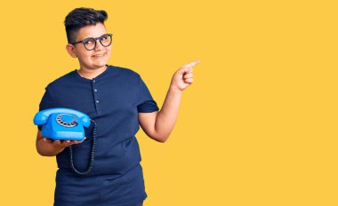 Klasik telefon kullanan küçük çocuk gülümsüyor mutlu bir şekilde elini ve parmağını yana doğru gösteriyor. 