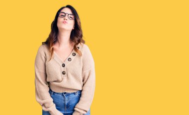 Güzel, genç, esmer bir kadın, günlük kıyafetler ve gözlük takmış kameraya bakıyor. Havada öpücük yolluyor. Sevimli ve seksi. aşk ifadesi. 