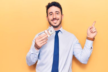 İş kıyafetleri giyen genç İspanyol adam dolarları tutuyor. Gülümsüyor, mutlu bir şekilde elini ve parmağını yana uzatıyordu. 