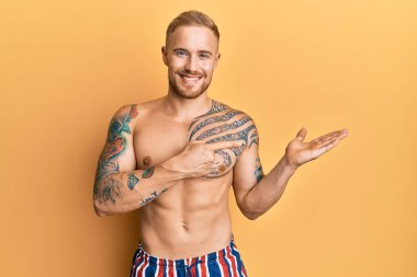 Mayo giyen genç beyaz adam hayrete düşmüş ve kameraya gülümsüyor. Elle ve parmakla işaret ediyor.. 