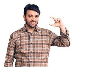 Gündelik kıyafetler giyen, gülümseyen, kendine güvenen, el hareketi yapan, parmaklarıyla işaret yapan ve kameraya bakan genç İspanyol bir adam. ölçüm kavramı. 