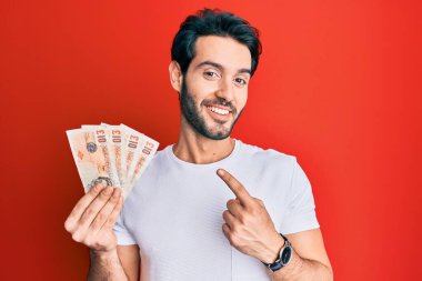 İspanyol asıllı genç adam, elinde 10 pound tutuyor. Banknotlar, mutlu bir şekilde parmakla işaret ediyor. 