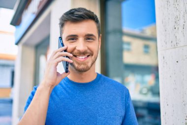 Genç beyaz adam gülümsüyor. Şehirdeki akıllı telefondan konuşuyor..