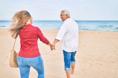 Orta yaşlı İspanyol çift kumsalda yürürken mutlu bir şekilde gülümsüyor..