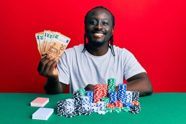 50 avroluk banknotlarla poker oynayan yakışıklı genç bir adam. Olumlu ve mutlu görünüyor. Kendine güvenen bir gülümsemeyle dişlerini gösteriyor. 