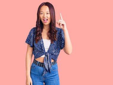 Gündelik giysiler giyen genç, güzel Çinli kız başarılı bir fikri işaret ediyor. Heyecanlı ve mutlu. Bir numara.. 