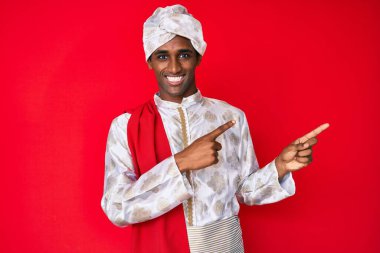 Gelenek giyinmiş yakışıklı Hintli adam Sherwani sari elbiseleri giyiyor gülümsüyor ve kameraya bakıyor iki eliyle ve parmaklarıyla kenarı işaret ediyor.. 