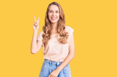 Sarı saçlı, sıradan kıyafetler giyen, kameraya bakıp zafer işareti yapan güzel beyaz bir kadın. İki numara.. 