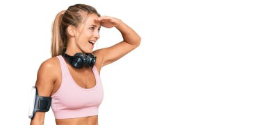 Genç sarışın kadın spor kıyafetleri giyiyor ve kulaklık takıyor. Çok mutlu ve gülümsüyor. Çok uzaklara bakıyor. arama kavramı. 