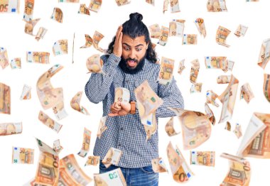 Gündelik giysiler giymiş genç bir Arap saati izliyor endişeli, geç kalmaktan korkuyor.