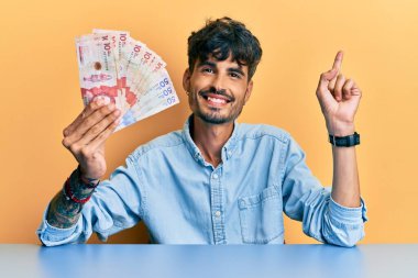 Elinde Kolombiya pezosu olan genç bir İspanyol adam masaya oturmuş gülümsüyor. 