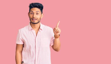 Gündelik tişört giyen yakışıklı Latin Amerikalı genç adam başarılı bir fikirle işaret ediyor. Heyecanlı ve mutlu. Bir numara.. 