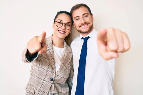 Beautiful couple wearing business clothes pointing to you and the camera with fingers, smiling positive and cheerful
