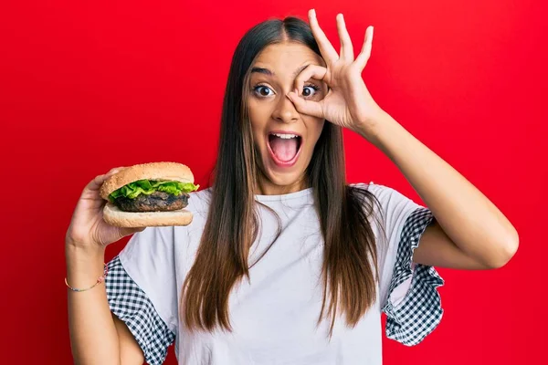Fiatal Spanyol Eszik Hamburger Mosolyog Boldog Csinál Rendben Jel Kéz — Stock Fotó