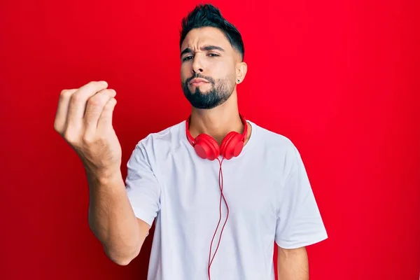 髭を生やした若い男は ヘッドフォンを使用して音楽を聴く手と指でイタリアのジェスチャーを行う自信を持って表現 — ストック写真