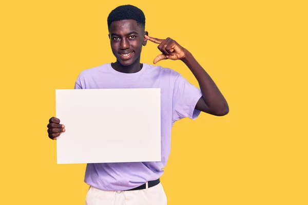 年轻的非洲裔美国人举着空白的横幅 指指点点着一个人 开心而自豪地微笑着 — 图库照片