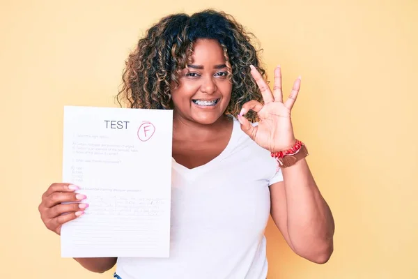 Young african american plus size woman showing a failed exam doing ok sign with fingers, smiling friendly gesturing excellent symbol