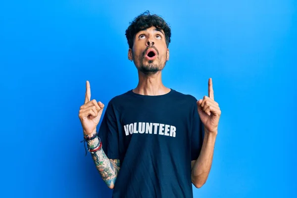 Jovem Hispânico Homem Vestindo Voluntário Shirt Espantado Surpreso Olhando Para — Fotografia de Stock