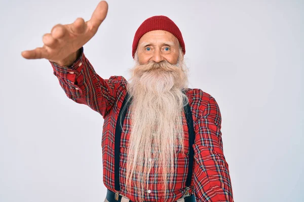 Old senior man with grey hair and long beard wearing hipster look with wool cap looking at the camera smiling with open arms for hug. cheerful expression embracing happiness.