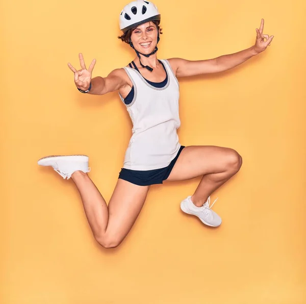 若い美しいバイカーの女性が幸せな笑顔自転車ヘルメットを着用 孤立した黄色の背景の上に顔に笑顔でジャンプ — ストック写真