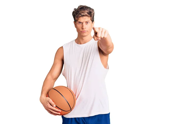 若いですハンサムな男保持バスケットボールボールポインティングとともに指でカメラとあなたに 自信を持ってジェスチャーを真剣に見て — ストック写真