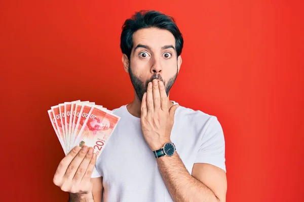 Young Hispanic Man Holding Israel Shekels Banknotes Covering Mouth Hand — Stock Photo, Image