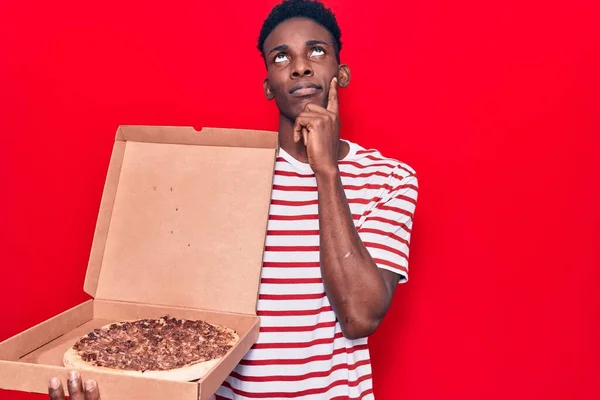 Mladý Africký Američan Držící Krabici Pizzy Vážný Obličej Přemýšlející Otázce — Stock fotografie