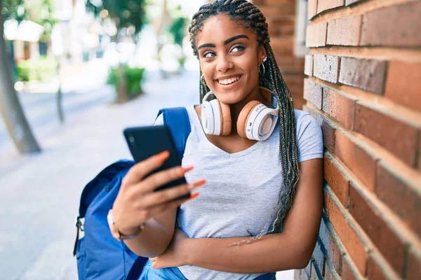 Genç Afrikalı Amerikalı öğrenci kampüste akıllı telefon kullanarak mutlu bir şekilde gülümsüyor.