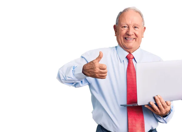 年长英俊的白发苍苍的男士打着领带 用笔记本电脑开心而积极地微笑着 大拇指向上翘起 做得出色 并签了字 — 图库照片