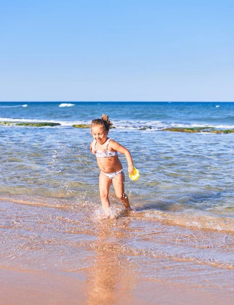 ビキニを着た愛らしい金髪の子供が笑顔で幸せ ビーチで水遊びをしながら笑顔で立って — ストック写真