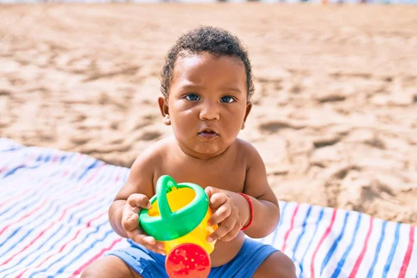 愛らしいアフリカ系アメリカ人の幼児はおもちゃで遊んでいます砂の上に座ってビーチ — ストック写真